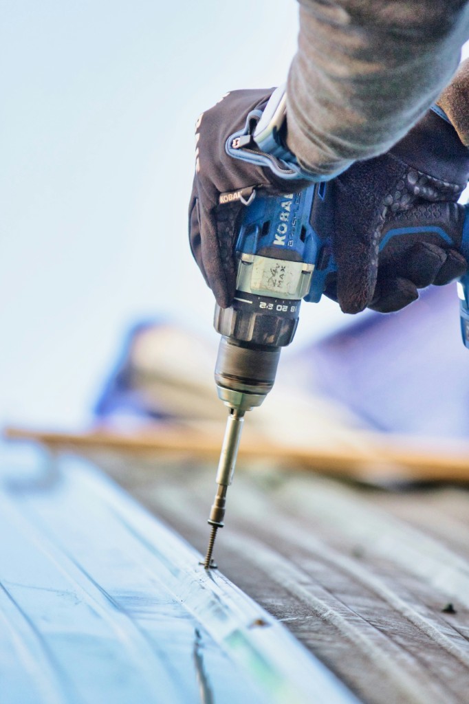 Roofer fastening metal roofing with a drill