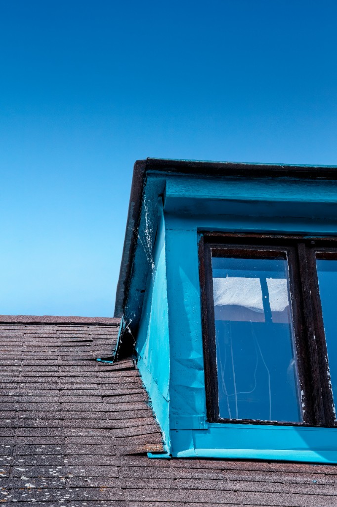 Blue dormer window on a shingled roof against a clear sky